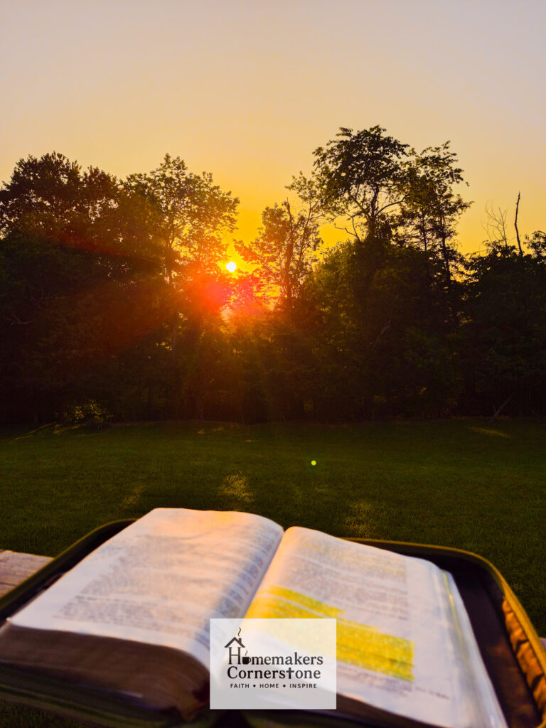 Picture of open bible on a porch rail with the sunrise in the background through the trees.